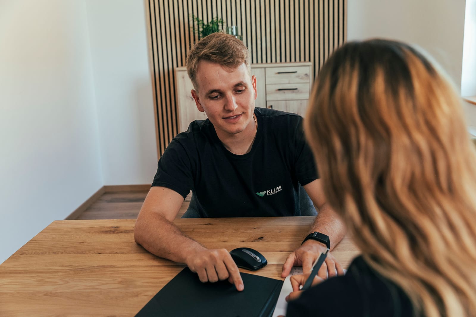 KLUW-Mitarbeiter geht mit einer Kundin am Besprechungstisch die Unterlagen zur Förderung durch