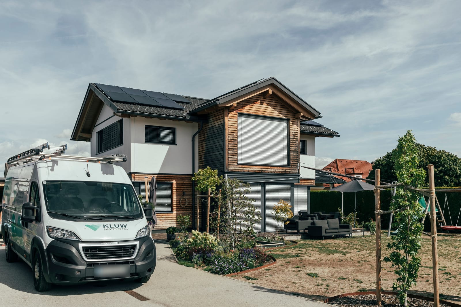 KLUW-Fahrzeug vor einem Einfamilienhaus mit fertiger PV-Anlage auf dem Dach