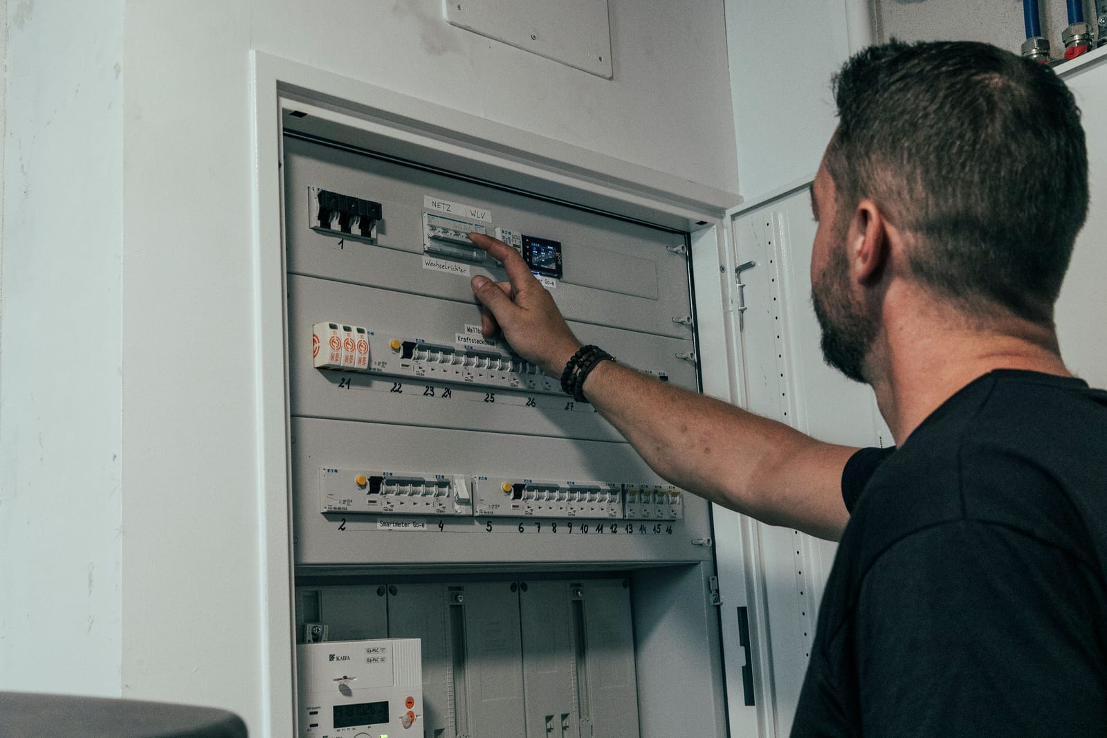 Techniker prüft die Sicherungen im offenen Zählerkasten, über die Schulter aufgenommen
